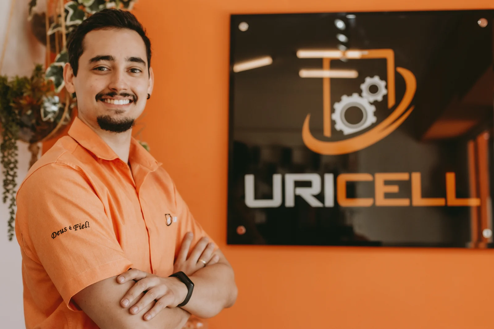 Proprietário da URICELL sorrindo, de braços cruzados, ao lado do letreiro da loja